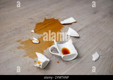 Eine kaputte Tasse Kaffee fiel auf Laminat, Kaffee verschüttete auf dem Boden. Stockfoto