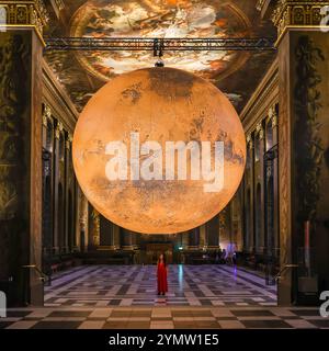 London, Großbritannien. November 2024. Das Personal posiert mit der Installation. Das Old Royal Naval College begrüßt Luke Jerrams beliebte beleuchtete Installation „Mars“ in der historischen Painted Hall. Die Installation wird ab heute bis zum 20. Januar 2025 ausgestellt. Quelle: Imageplotter/Alamy Live News Stockfoto