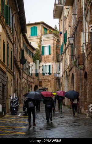 Blick auf Touristen, die in einer engen und gemütlichen Straße in der Altstadt von Siena in Italien spazieren. Konzept der antiken Architektur der toskanischen Region. Siena Stockfoto