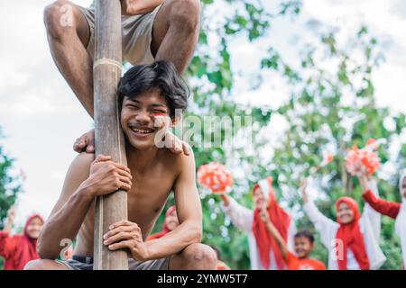 Der Mensch lacht, während er das Gewicht trägt, die Areca-Nuss zu erklimmen, um Indonesiens Unabhängigkeit zu feiern Stockfoto