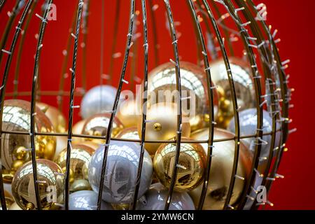 Viele farbenfrohe Weihnachtskugeln in einem Metallkorb, der mit Girlande verziert ist Stockfoto