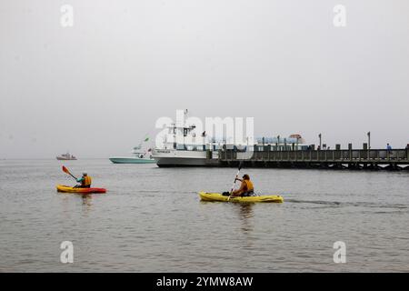 Fire Island, New York, USA - 9. Juli 2024: Kajakfahrer genießen ein friedliches Paddeln an einem nebeligen Tag, umgeben von ruhigem Wasser und Booten am Dock. Stockfoto