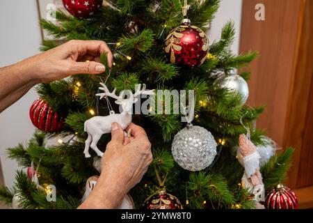 Eine Person schmückt einen Weihnachtsbaum mit einem Hirschschmuck und anderen Ornamenten. Der Baum ist voller Dekorationen, darunter eine große Anzahl von roten und Stockfoto