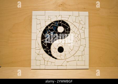 Ein Yin-Yang-Symbol in Mosaikform, hergestellt aus Keramikfliesen und Fliesenfugen. Der Moasäer lehnt sich auf ein Stück Sperrholz, nachdem bing fertig ist. Stockfoto