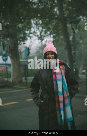 Eine Frau steht auf einer belebten Straße und trägt einen stylischen rosa Hut und Schal Stockfoto