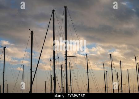 Feurige kontrastierende Wolken am blauen Himmel, bei Sonnenuntergang, durch die Masten von Segelyachten. Stockfoto