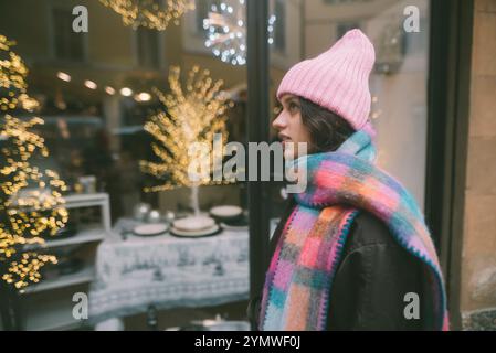 Eine Frau mit rosa Mütze und passendem Schal schaut auf ein Schaufenster Stockfoto