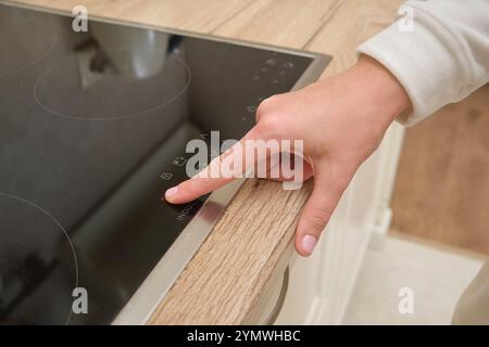 Drücken Sie mit der Hand die ein-/Ausschalttaste auf dem Induktionskochfeld. Blick aus der Nähe in einer modernen Küche. Technologie- und Küchengerätekonzept für Design und Prin Stockfoto