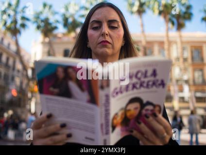 Malaga, Spanien. November 2024. Eine Aktivistin sieht sich ein Buch an, während sie an einer Performance zum Internationalen Tag zur Beseitigung von Gewalt gegen Frauen auf der Plaza de la Constitucion teilnimmt. Aktivisten und Freiwillige der Nichtregierungsorganisation Prodiversa nahmen an einer künstlerischen und theatralischen Aktivität Teil, die von der Künstlerin und Performerin Verónica Ruth Frías organisiert wurde, um geschlechtsspezifische Gewalt anzuprangern. Dieser künstlerische Vorschlag vereint Kunst und Aktivismus. Quelle: SOPA Images Limited/Alamy Live News Stockfoto