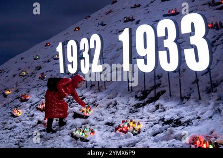 Kiew, Ukraine. November 2024. Person, die eine Kerze auf einem Hügel mit brennenden Kerzen am Holodomor Opfer Gedenktag am Holodomor Opfer Gedenktag zündet. Die großen Buchstaben 1932 bis 1933 symbolisieren die Zeit des Holodomors. Während des Holodomors verhungerten Millionen Ukrainer aufgrund einer von Menschen verursachten Hungersnot. Jeden 4. Samstag im November um 4 Uhr werden die Kerzen in der ganzen Ukraine gezündet. Quelle: Andreas Stroh/Alamy Live News Stockfoto