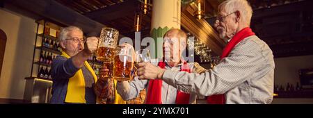 Ältere Menschen, Männer in farbenfrohen roten und gelben Tüchern treffen sich in einer Bar, einem Pub, klirrrenden Bierbecher und feiern den Sieg der Lieblingsmannschaft Stockfoto