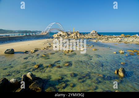 Yangyang County, Südkorea - 3. November 2024: Kristallklares Gezeitenwasser und Felsvorsprünge umgeben die Bogenbrücke und den gelben Leuchtturm bei N Stockfoto