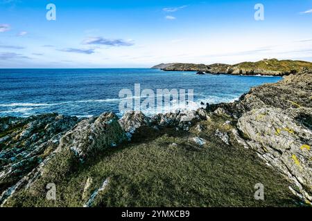 Die Sonne untergeht über dem Horizont und beleuchtet die zerklüfteten Klippen am ruhigen Meer. Wellen schlagen sanft gegen die Felsen und schaffen eine friedliche Küste Stockfoto