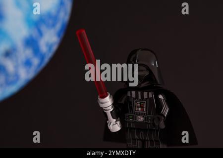 Tambow, Russische Föderation - 14. November 2024 Lego Darth Vader Minifigur mit Lichtschwert auf schwarzem Hintergrund mit blauem Planeten Stockfoto