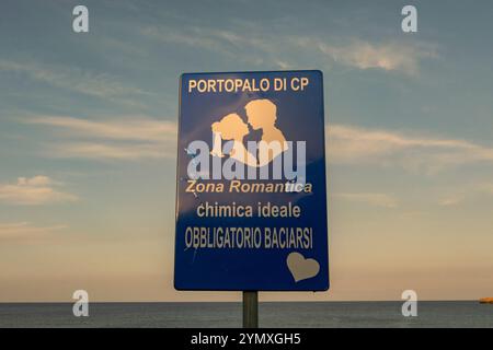 Ein Schild mit der Aufschrift „Kuss hier - Ort für romantische Fotos“ mit Blick auf das Mittelmeer in der kleinen Küstenstadt Portopalo di Capo Passero. Stockfoto