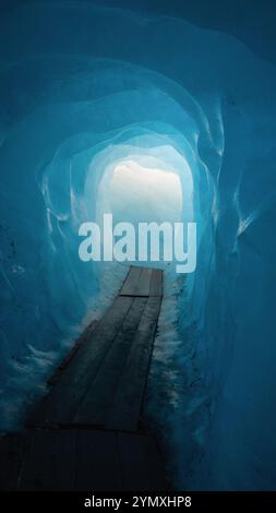 Innerhalb Des Rhône-Gletschers. Licht am Ende der blauen Eisgrotte. Holzsteg in einem Tunnel in einem Gletscher. Stockfoto