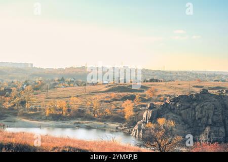 Eine exquisite Herbstlandschaft mit lebendigem, farbenfrohem Laub, einem friedlichen und ruhigen Fluss, der sanft fließt, verstreute zerklüftete Steine auf dem Boden, alles unter einem atemberaubend klaren blauen Himmel Stockfoto