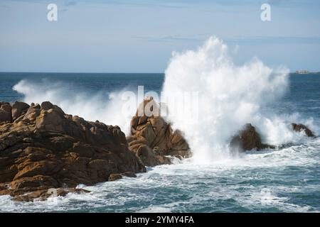 Dramatische Wellen, die in einem blauen Ozean unter klarem Himmel gegen Felsen stürzen, Ploumanac'h, Ploumanach, Perros-Guirec, Cotes-d'Armor, Bretagne, Frankreich, Eur Stockfoto