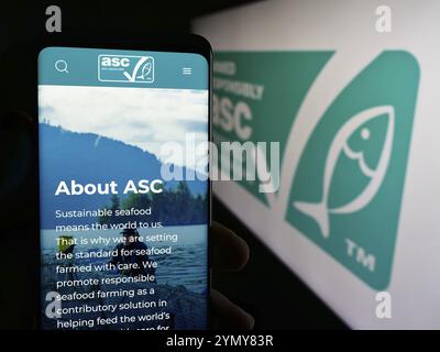 Stuttgart, Deutschland, 07.01.2024: Person mit Handy und Website der Organisation Aquaculture Stewardship Council (ASC) vor dem Logo. Konzentrieren Sie sich auf Stockfoto