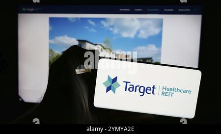 Stuttgart, Deutschland, 29.05.2024: Person mit Handy mit Logo des britischen Immobilienunternehmens Target Healthcare REIT vor der Business-Webseite. Fo Stockfoto