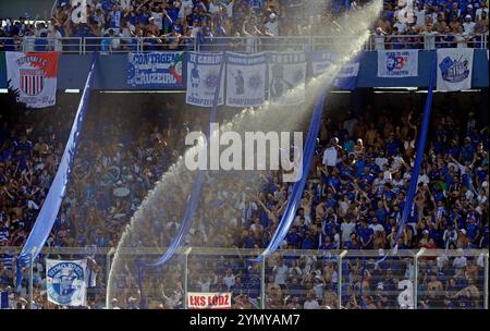 Die Fans des argentinischen Racing Clubs werden mit Wasser besprüht, während sie auf den Start des Finalspiels der CONMEBOL Copa Sudamericana gegen den brasilianischen Cruzeiro im La Nueva Olla Stadion in Asuncion, Paraguay, am 23. November 2024 warten. Stockfoto