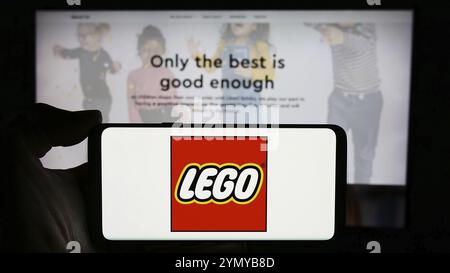 Stuttgart, Deutschland, 04.02.2024: Person, die ein Mobiltelefon mit dem Logo des dänischen Bauspielzeugherstellers LEGO hält, WIE vor der Webseite. Fokus auf p Stockfoto