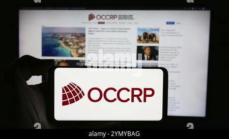 Stuttgart, 22.05.2024: Person, die ein Mobiltelefon mit dem Logo des "Organized Crime and Corruption Reporting Project" (OCCRP) vor der Webseite hält. Fo Stockfoto