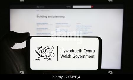 Stuttgart, Deutschland, 25.03.2024: Person mit Handy mit Logo der walisischen Regierung (Llywodraeth Cymru) vor der Webseite. Schwerpunkt auf dem Display des Telefons Stockfoto