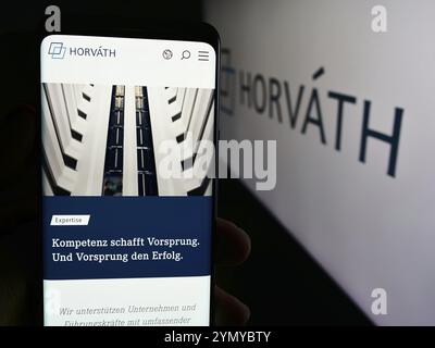 Stuttgart, 15.07.2024: Handybesitzer mit Webseite der deutschen Unternehmensberatung Horvath AG vor Logo. Fokus auf ce Stockfoto