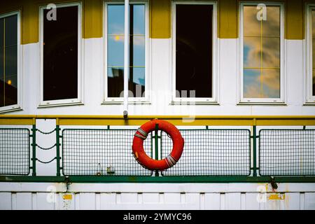 Leuchtend roter Lifebuoy, montiert auf einer bunten Schiene mit industriellem Hintergrund Stockfoto