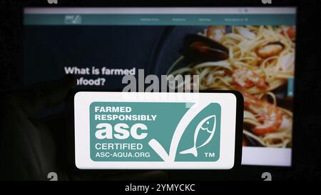 Stuttgart, Deutschland, 07.01.2024: Person mit Handy mit Logo der Organisation Aquaculture Stewardship Council (ASC) vor der Webseite. Konzentrieren Sie sich auf Stockfoto