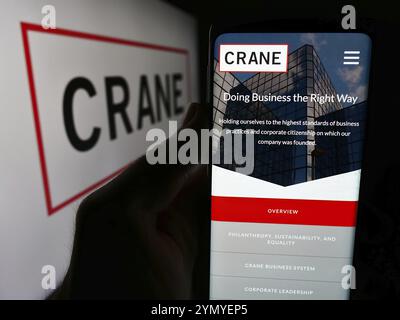 Stuttgart, Deutschland, 07.04.2024: Person, die ein Mobiltelefon hält, mit Webseite des US-amerikanischen Industrieunternehmens Crane Co. Vor dem Firmenlogo. Konzentrieren Sie sich auf Stockfoto