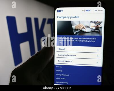 Stuttgart, Deutschland, 13.04.2024: Person, die ein Smartphone mit Webseite des Telekommunikationsunternehmens HKT Limited (Hong Kong Telecom) mit Logo hält. Fokus Stockfoto