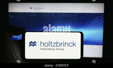 Stuttgart, 22.05.2024: Handybesitzer mit Logo des deutschen Medienunternehmens Holtzbrinck Publishing Group vor der Business-Webseite. Stockfoto