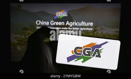 Stuttgart, Deutschland, 28.04.2024: Person, die ein Mobiltelefon mit dem Logo des chinesischen Unternehmens China Green Agriculture Inc. (CGA) vor der Unternehmenswebsite hält Stockfoto