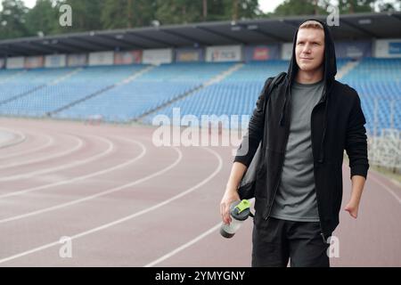 Porträt eines sportlichen jungen Mannes, der auf der Laufstrecke steht und die Sportflasche in einer Hand hält Stockfoto