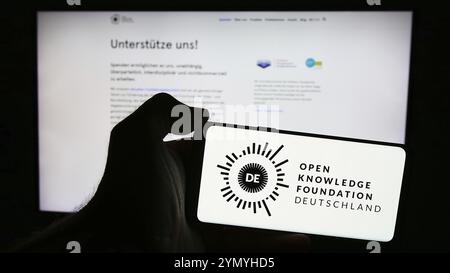 Stuttgart, 21.05.2024: Person mit Handy mit Logo der Open Knowledge Foundation Deutschland e.V. (OKFDE) vor der Webseite. Konzentrieren Sie sich auf Stockfoto