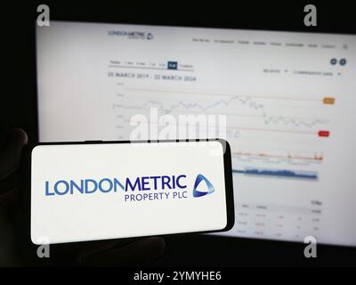 Stuttgart, Deutschland, 25.03.2024: Person, die ein Mobiltelefon mit dem Logo der britischen Immobiliengesellschaft LondonMetric Property plc vor der Webseite hält. F Stockfoto