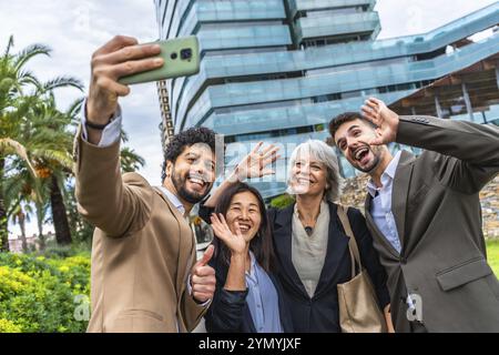 Eine vielfältige und ethnische Gruppe eleganter Geschäftsleute, die vor der Kamera winkten, während sie ein Selfie mit einem Smartphone machen, das in einem Finanzviertel steht Stockfoto