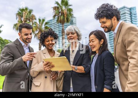 Reife Geschäftsfrau, die ein digitales Tablet nutzt, während sie sich während eines Meetings im Freien mit multiethischen Geschäftskollegen unterhält Stockfoto