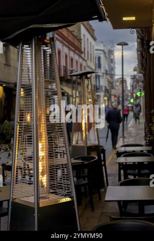 Auf der Terrasse einer Bar in einer Fußgängerzone im Hintergrund laufen die Butanöfen in Flammen vorbei Stockfoto