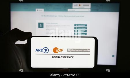 Stuttgart, Deutschland, 04.10.2024: Handybesitzer mit Logo des ARD ZDF Deutschlandradio Beitragsservice vor der Webseite. Konzentrieren Sie sich auf die Telefondiskretion Stockfoto