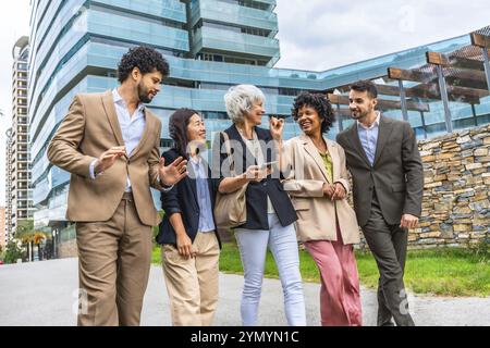 Multiethnische Geschäftsleute unterhielten sich entspannt beim Spaziergang durch das Finanzviertel in einer tropischen modernen Stadt Stockfoto