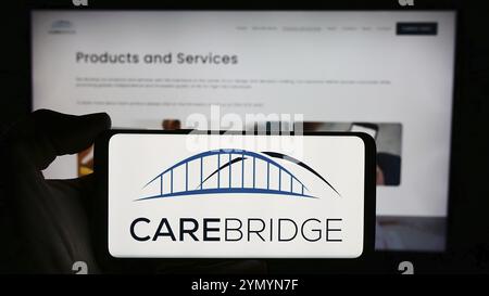 Stuttgart, Deutschland, 27.03.2024: Person mit Handy mit Logo des US-Gesundheitsunternehmens CareBridge vor der Business-Webseite. Konzentrieren Sie sich auf Telefon d Stockfoto