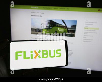 Stuttgart, Deutschland, 03.05.2024: Person mit Mobiltelefon mit Logo des deutschen Fernbusunternehmens FlixBus vor Business Web PA Stockfoto