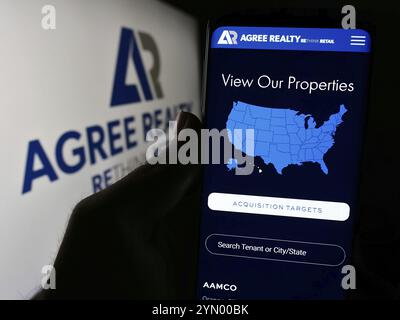 Stuttgart, Deutschland, 28.04.2024: Person, die ein Mobiltelefon hält, mit Webseite der US-Immobiliengesellschaft stimmt Realty Corporation vor dem Logo überein. Fokus auf ce Stockfoto