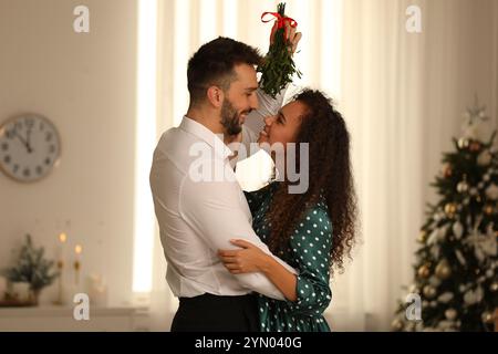 Ein reizendes Paar unter Mistelzweigen im Zimmer, das zu Weihnachten dekoriert war Stockfoto