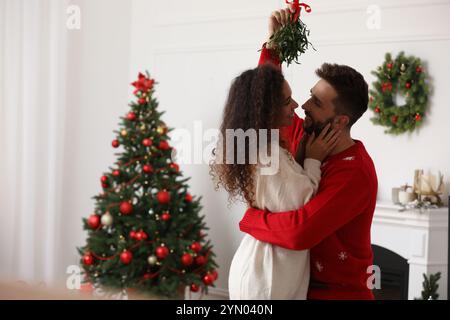 Ein reizendes Paar unter Mistelzweigen im Zimmer, das zu Weihnachten dekoriert war Stockfoto