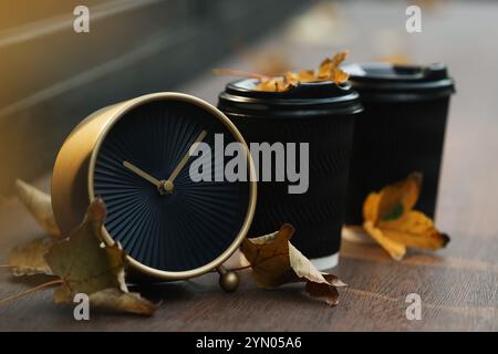 Herbstzeit. Wecker, gefallene Blätter und Tassen mit heißen Getränken im Freien, Platz für Text Stockfoto