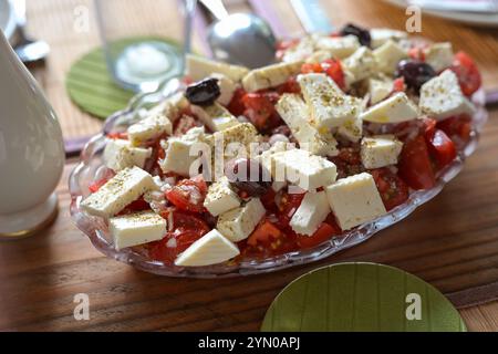 Salat im griechischen Stil mit Tomaten, Fetakäse, Zwiebeln und Oliven auf einem rustikalen Holztisch, geeignet für eine mediterrane Dinner Party, ausgewählte Fokussierung Stockfoto